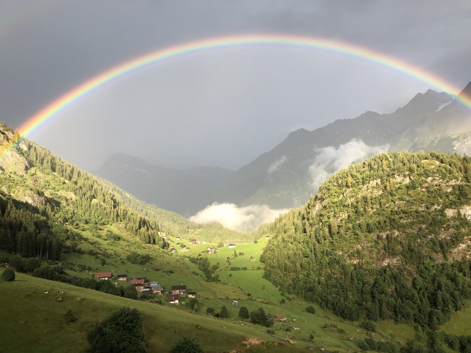 Regenbogen in einem grünen Bergtal.