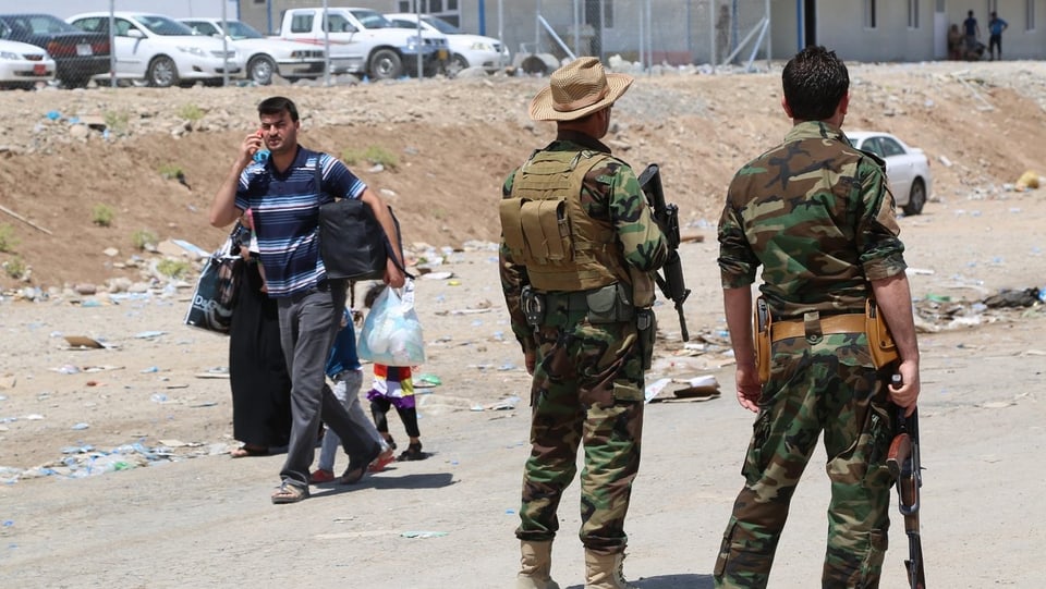 Ein Mann mit Frau und Kind, Plastiktüte in der Hand und Handy am Ohr, geht an zwei Soldaten vorbei.