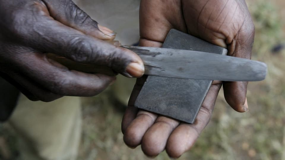 Hände eines afrikanischen Mannes halten ein Messer und einen Schleifstein für die rituelle Beschneidung.