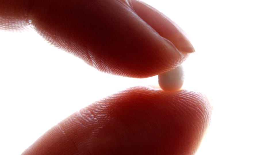 Eine Frau hält eine kleine Pille zwischen Daumen und Zeigefinger.