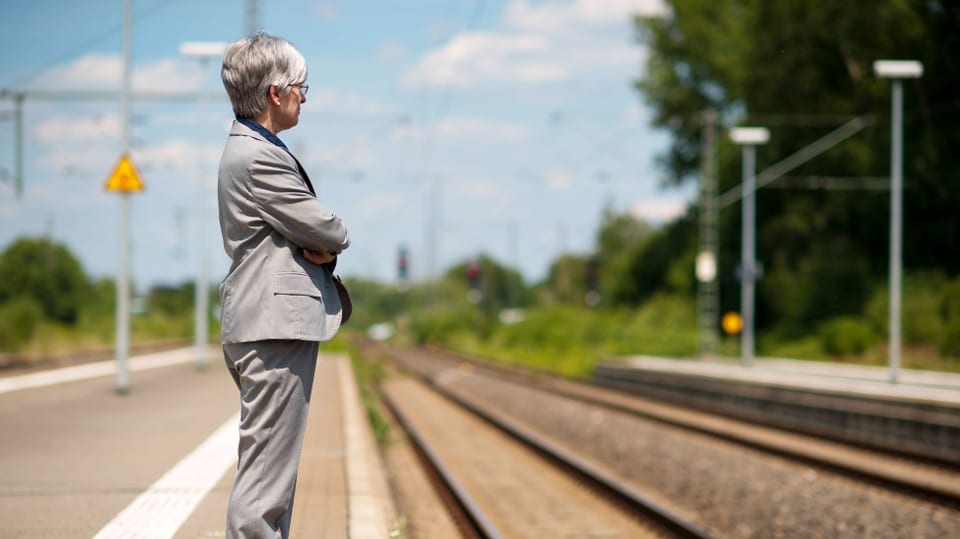Frau im mittleren Alter steht neben einem Bahngleis.