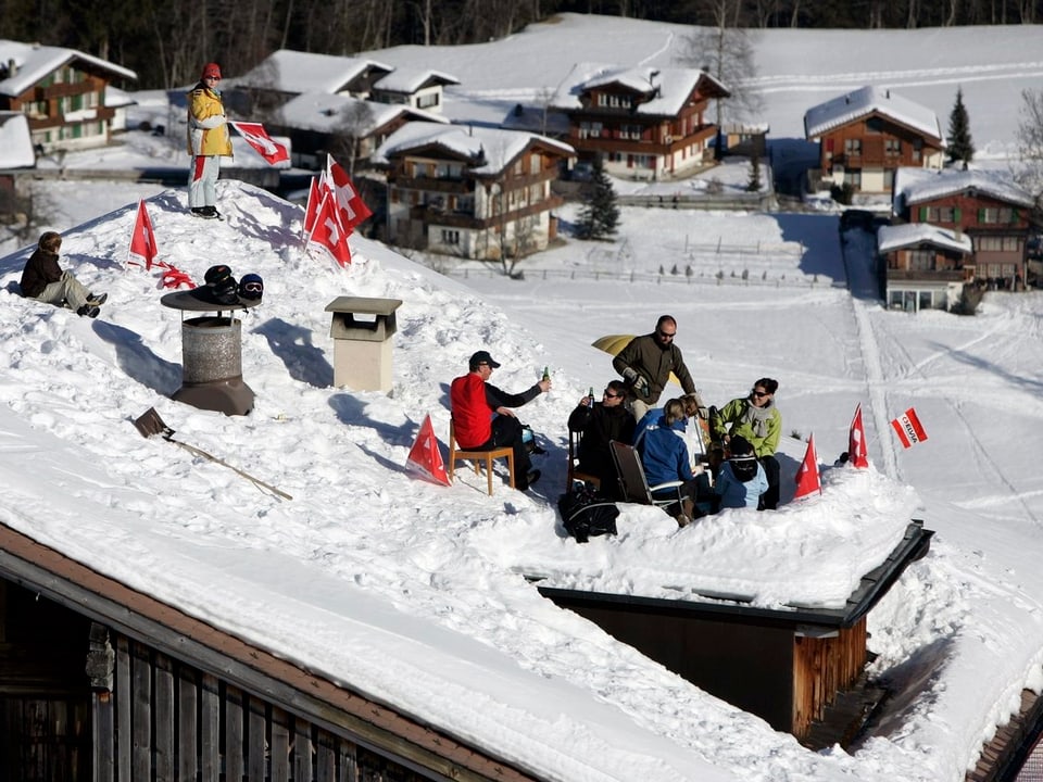 Menschen auf einem verschneiten Dach in Adelboden verfolgen das Skirennen.