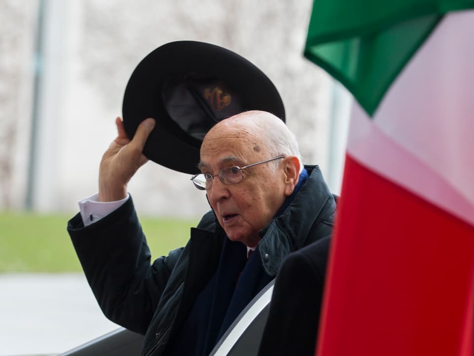 Napolitano hebt vor einer italienischen Flagge den Hut.