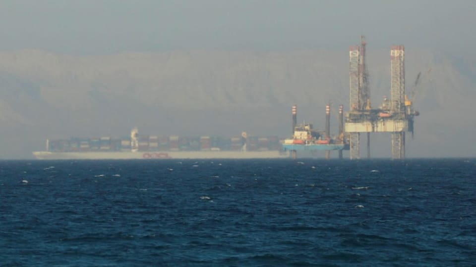 Schiff fährt an einer Ölplattform auf dem Meer vorbei.