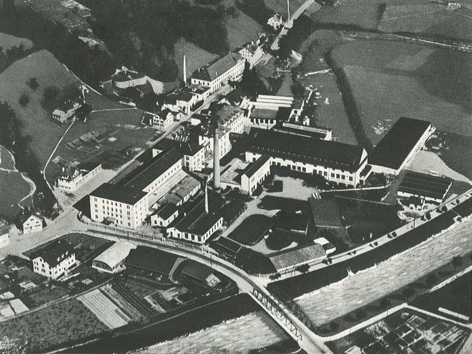Das Bild zeigt die Fabrik aus der Luft mit einem grossen Kamin und den länglichen Gebäuden rundum.