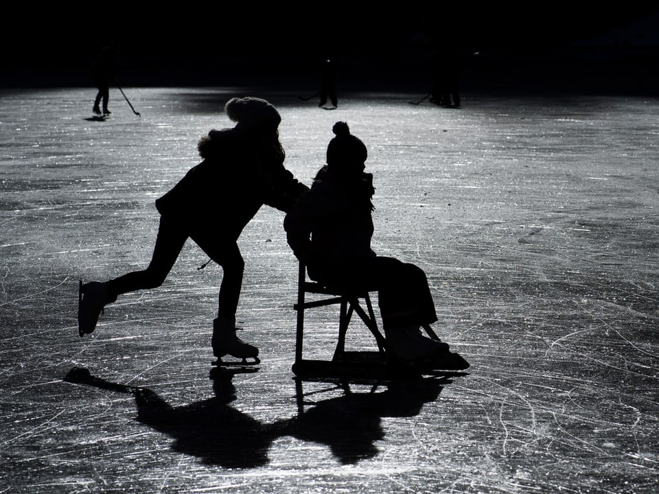 Eine Person schiebt eine Person auf einem Stuhl übers Eis.