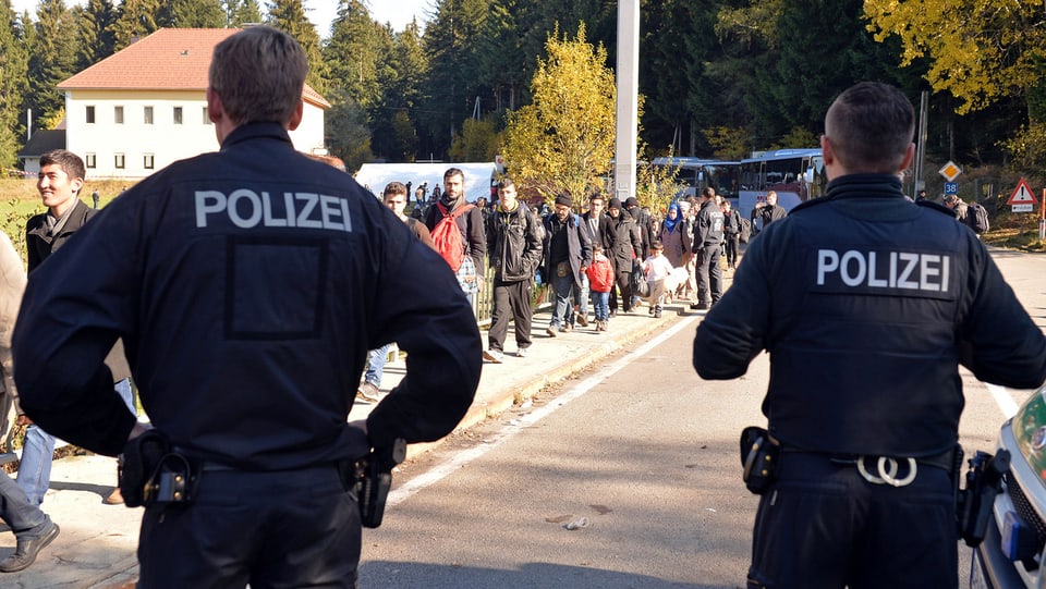 Zwei deutsche Polizisten beobachten eine Gruppe von Flüchtlingen.