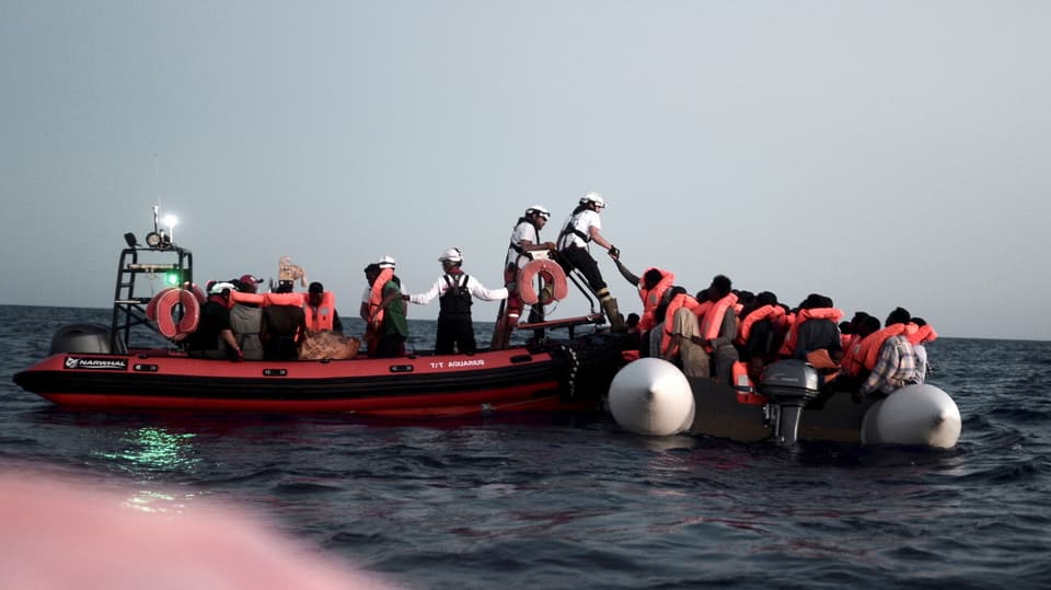 Ein Rettungsboot hilft Flüchtlingen um von ihrem Schlauchboot auf ein grösseres Gefährt zu wechseln.
