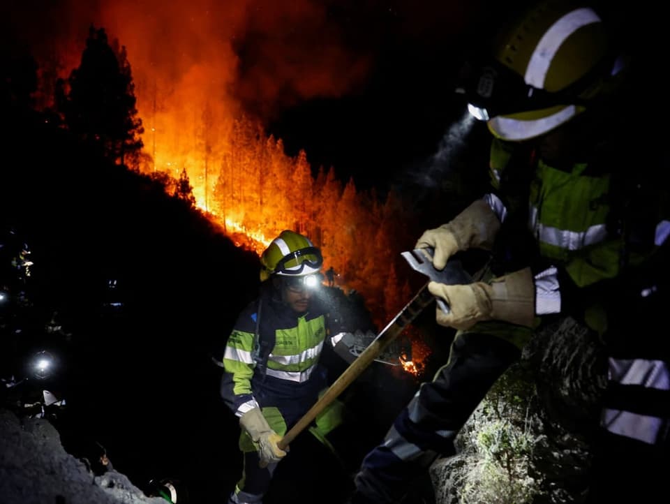 Feuerwehrleute vor einem Waldbrand mit leuchtenden Stirnlampen.