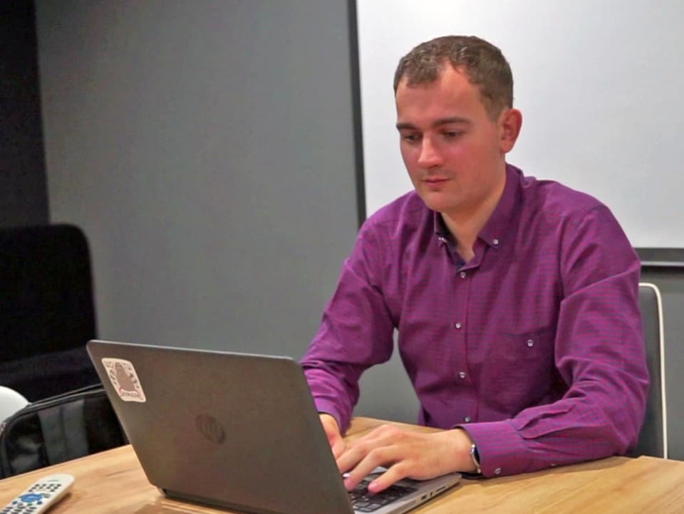 Ein Mann in einem lila Hemd sitzt an einem Laptop.