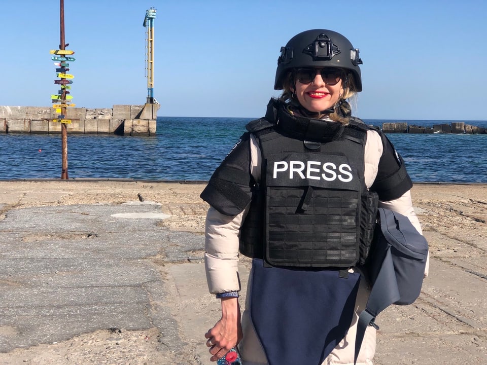 Luzia Tschirky steht an einer Uferpromenade mit Helm und Presse-Veste. Sie lächelt.