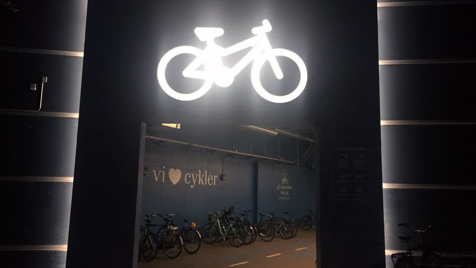 Velokeller bei Nacht. Darüber leuchtet ein Neon-Velo.