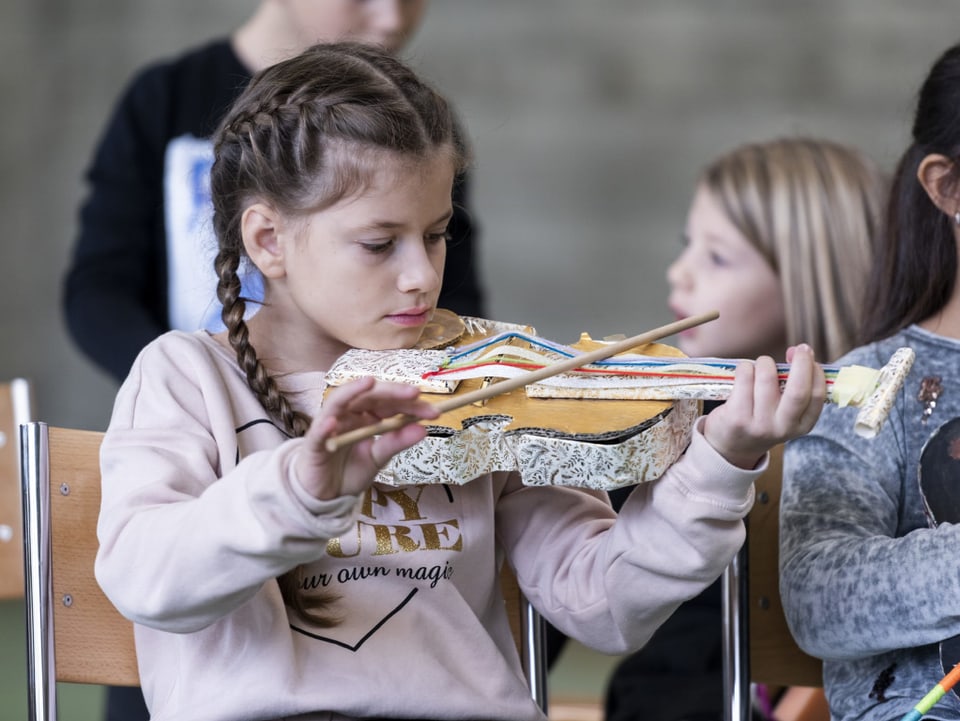 Mit einem Holzstab streicht ein Mädchen über die Wollsaiten ihres Papierinstruments.