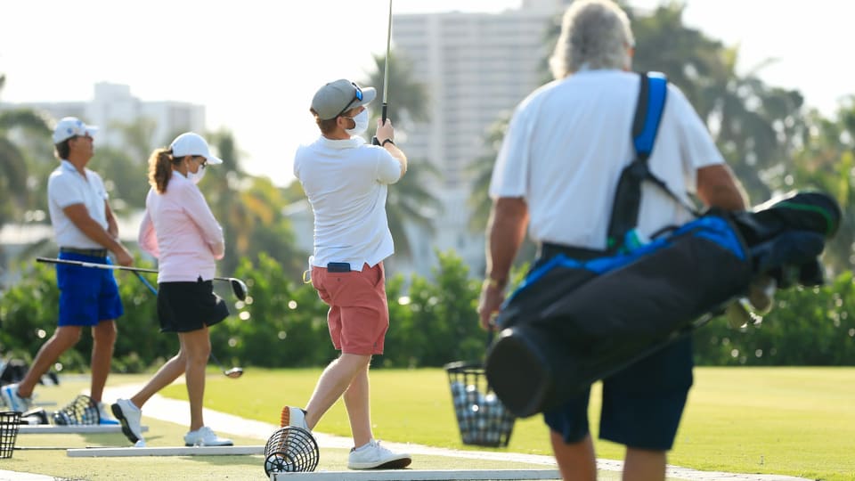 Golfer spielen auf der Driving Range Bälle und tragen Schutzmasken.