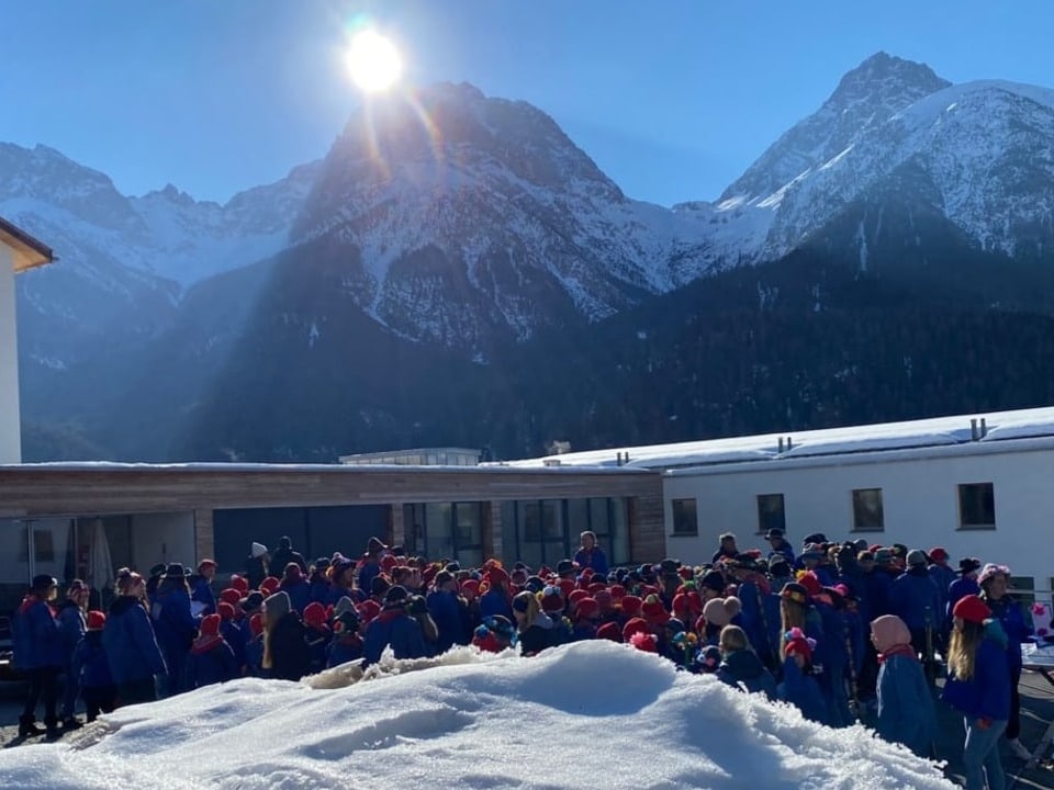 Einige Schulklassen stehen in einer Gruppe beieinander. Im Hintergrund sieht man die Berge. Alle sind blau gekleidet.