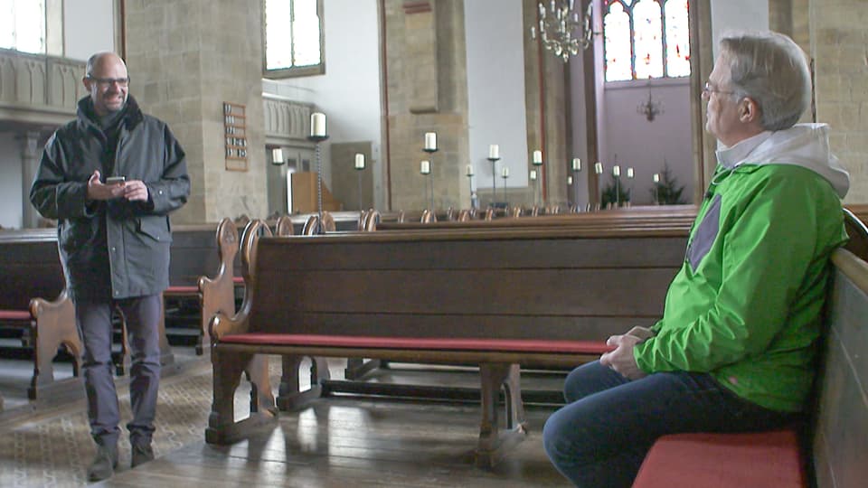 Mindens Pfarrer Frieder Küppers sitzt in seiner Kirche (weltlich bekleidet mit grüner Outdoor-Jacke) und tippt eine «gute Botschaft in sein Handy.