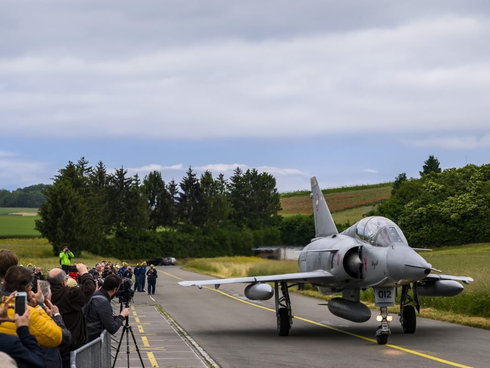 Menschen stehen am Rand des Rollfelds und fotografieren den Mirage-jet