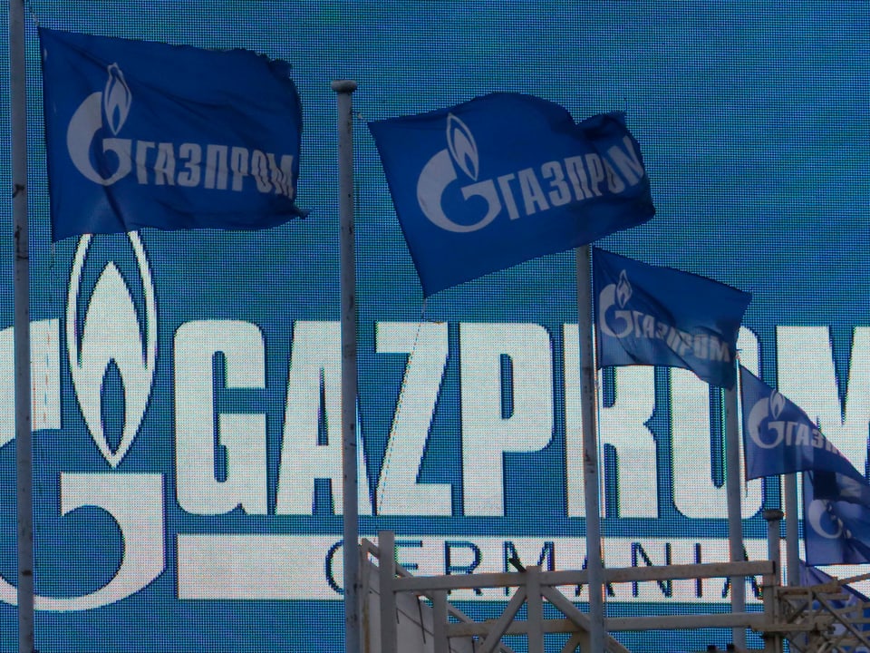 Flaggen vor einem Logo von Gazprom.