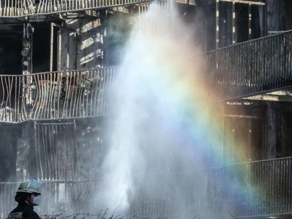 Ein Feuerwehrmann spritzt aus seiner Wasserspritze auf ein Gebäude.
