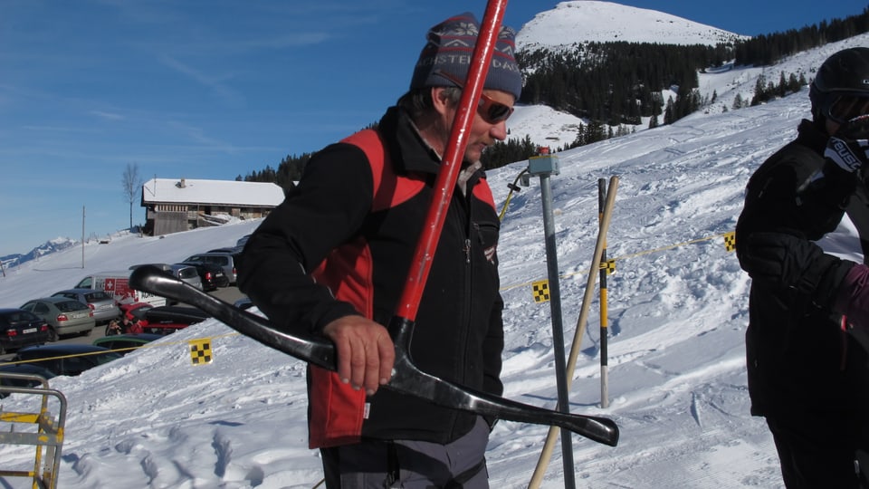 Ein sonniger Tag im Ski-Gebiet Elisgen-Metsch. Ueli Schütz mit Wollmütze und Sonnenbrille hält den Skiliftbügel in den Händen, um ihn dem nächsten Skifahrer zu übergeben.