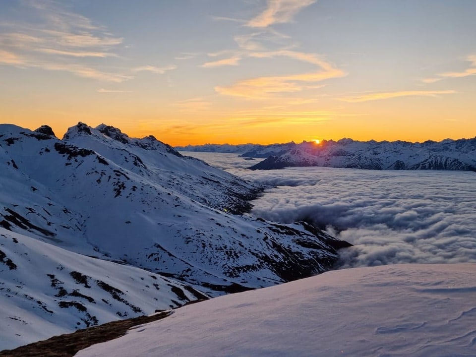 Sonnenaufgang über Alpental mit Schnee gefüllt mit Nebel. Darüber klarer Himmel.