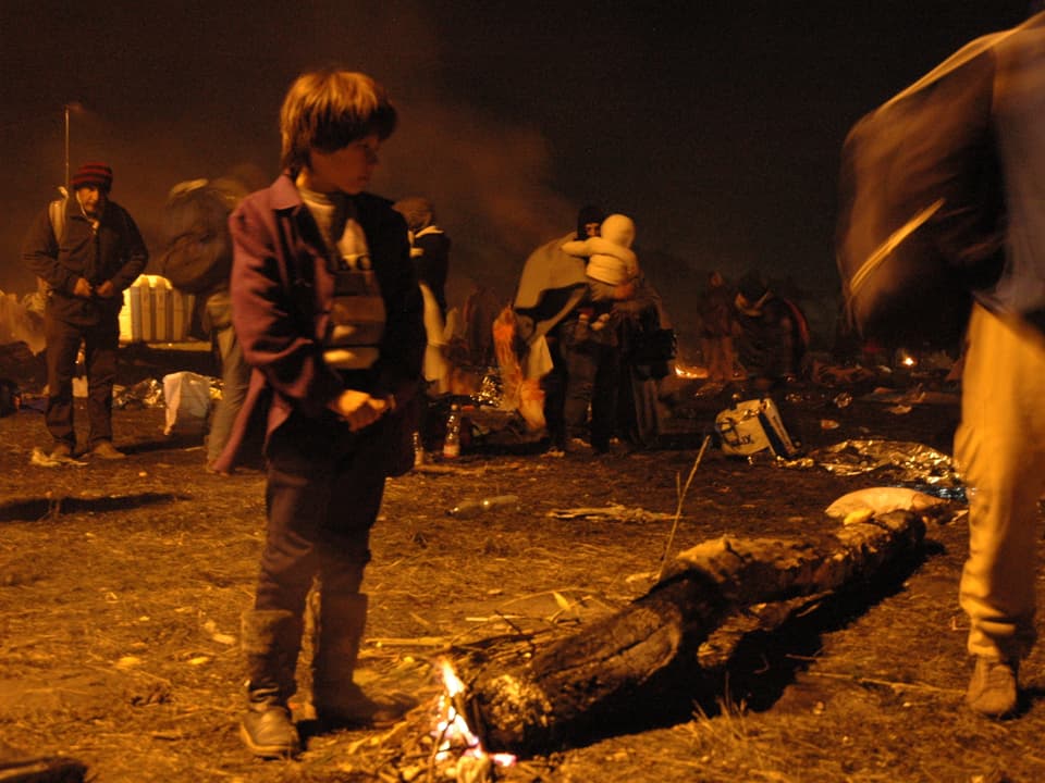 Ein Junge wärmt sich an einem brennenden Ast auf.