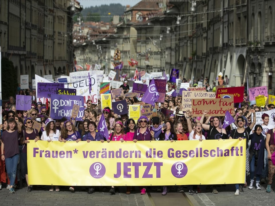 Demonstrationszug, vorne Plakat mit Aufschrift "Frauen verändern die Gesellschaft. Jetzt."