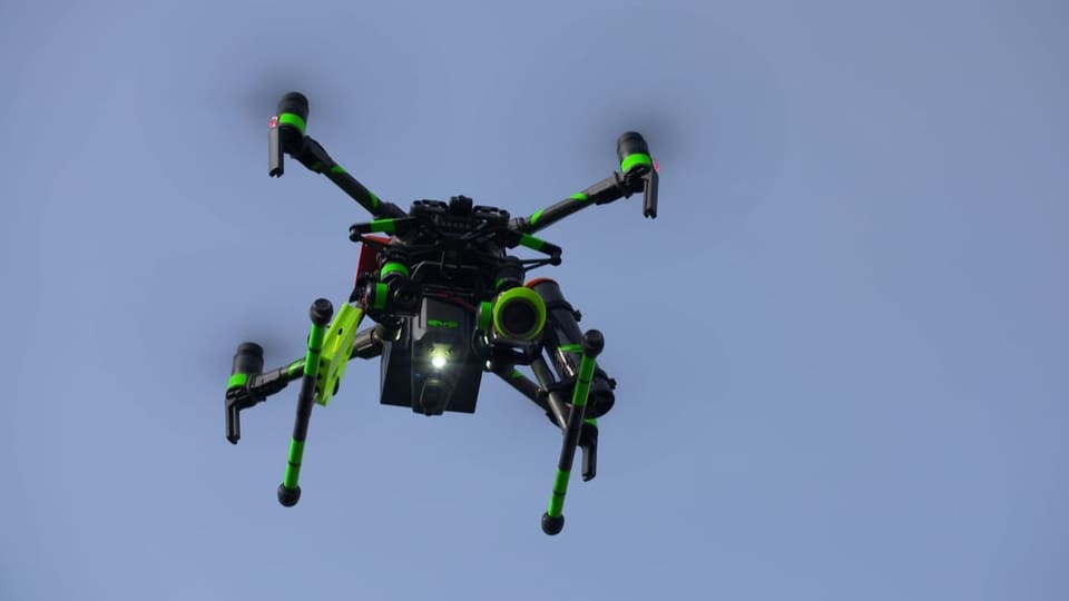 Auf dem Bild ist die grün-schwarze Drohne bei der Arbeit in der Luft zu sehen.