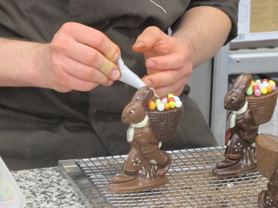 Die Schokoladehasen sind trocken und werden nun mit einem Spritzsack und Zuckereier verziert.