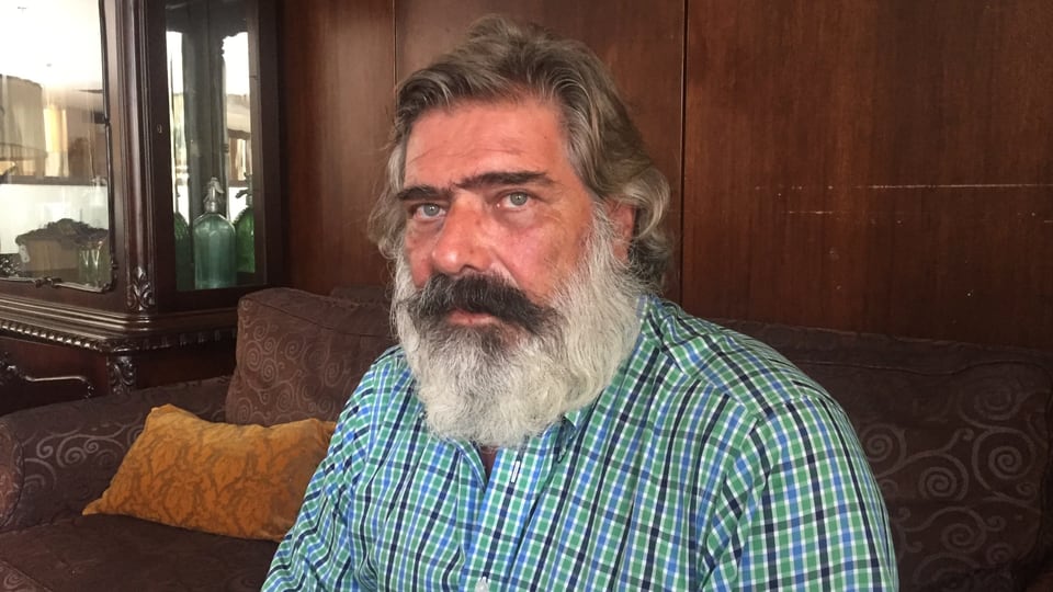 Nikos Giannopoulos, ein Mann mit schwarz-grauem Vollbart, auf einem Sofa.