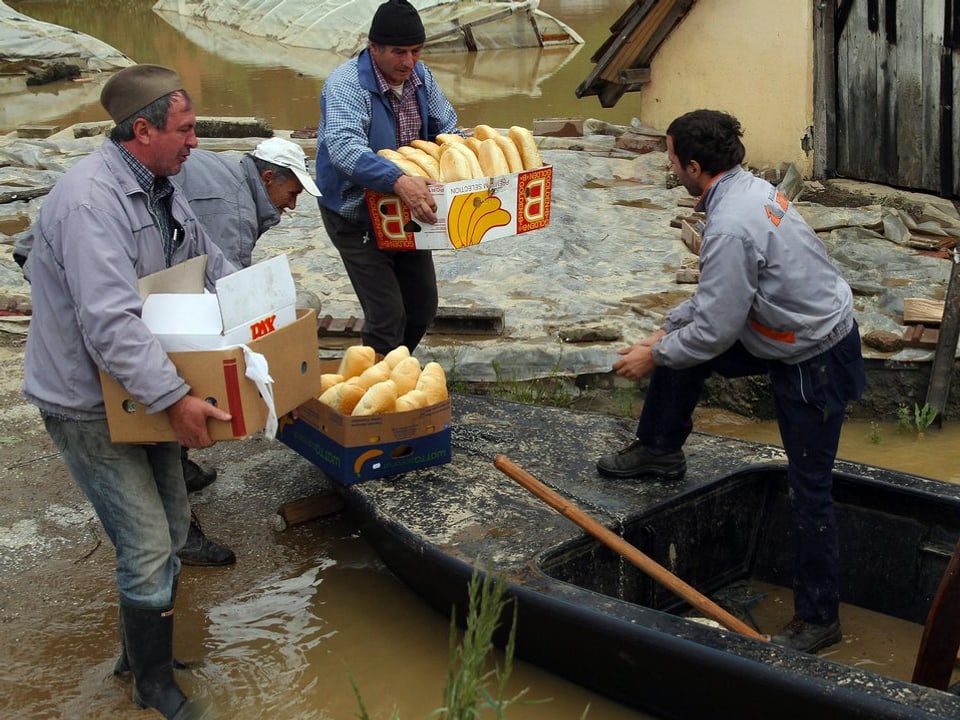Zwei Männer reichen einem Dritten Kartons voll Brot in ein Boot.