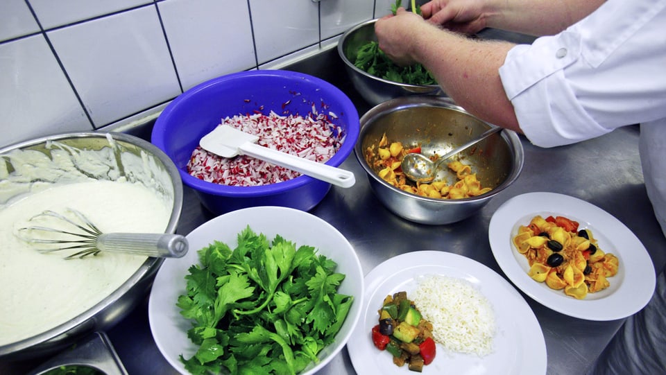 Ein Koch bereitet in der Küche ein Menü zu mit viel Gemüse und Salat.