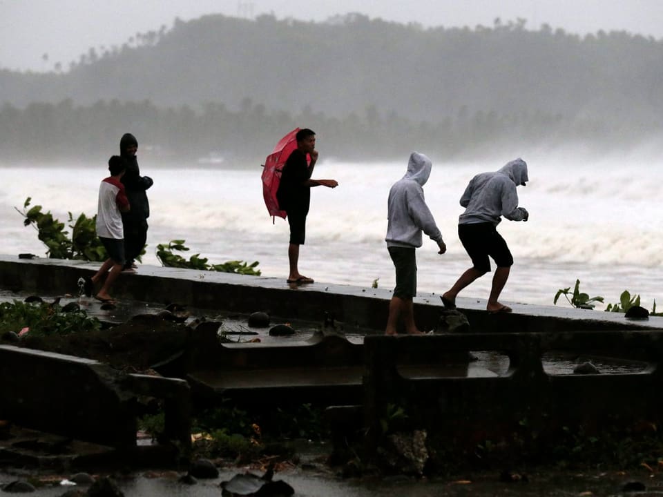 Mehrere junge Männer stehen an der Küste und betrachten die Wellen. 