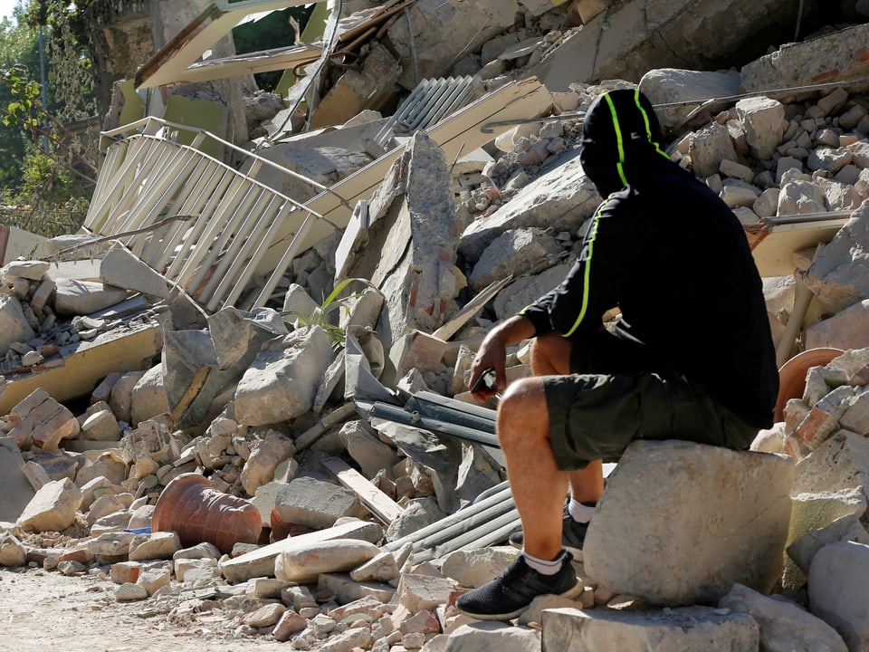 Eine Person hockt auf einem Stein vor einem Trümmerhaufen.
