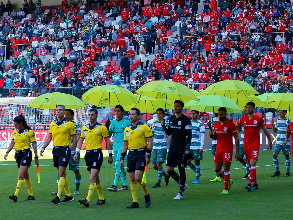 Spieler von Santos und Toluca halten Regenschirme in der Hand und stehen in Reihe und Glied.