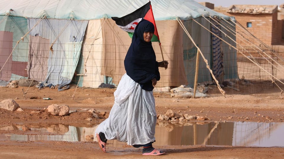 Eine Frau in einem Flüchtlingscamp an der algerischen Grenze hält eine Fahne, hinter ihr Zelte.