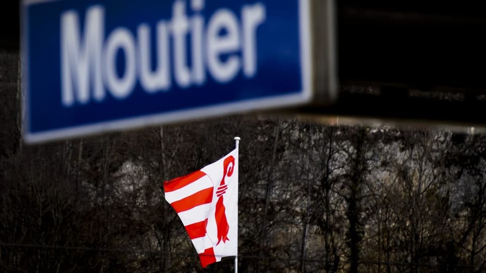 Eine Jura-Fahne weht unter dem Bahnhofschild von Moutier.