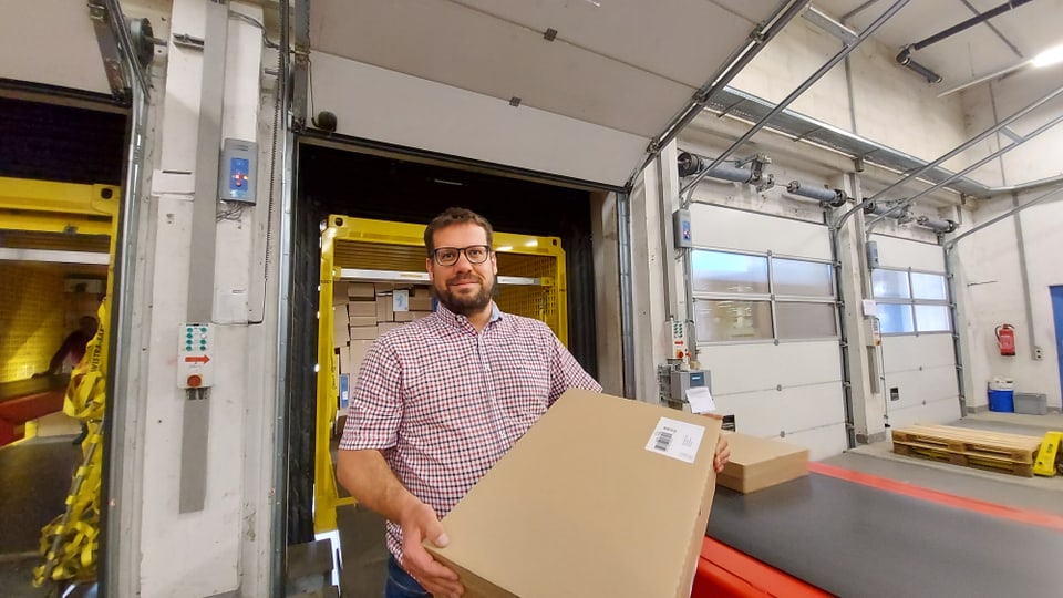 Steiger steht mit einem Paket in den Händen vor dem Fliessband.