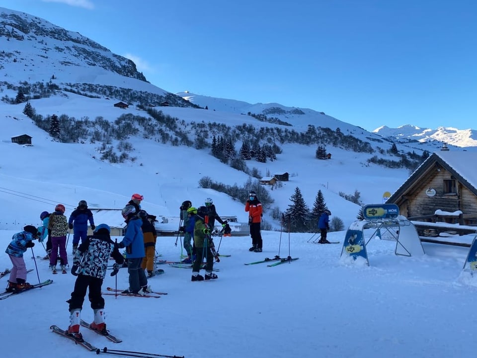 Gruppe von Kindern, die ihre Skis anzieht. Morgenstimmung, Landschaft und Schatten.