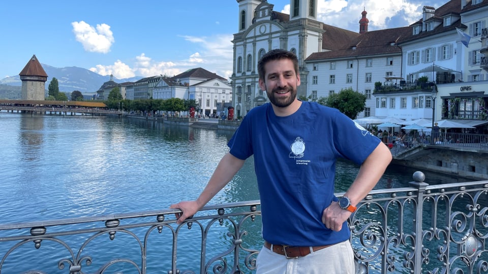 Jonas Amherd posiert auf einer Brücke, im Hintergrund ist eine Kirche zu sehen. Er trägt ein Jubla-T-Shirt.