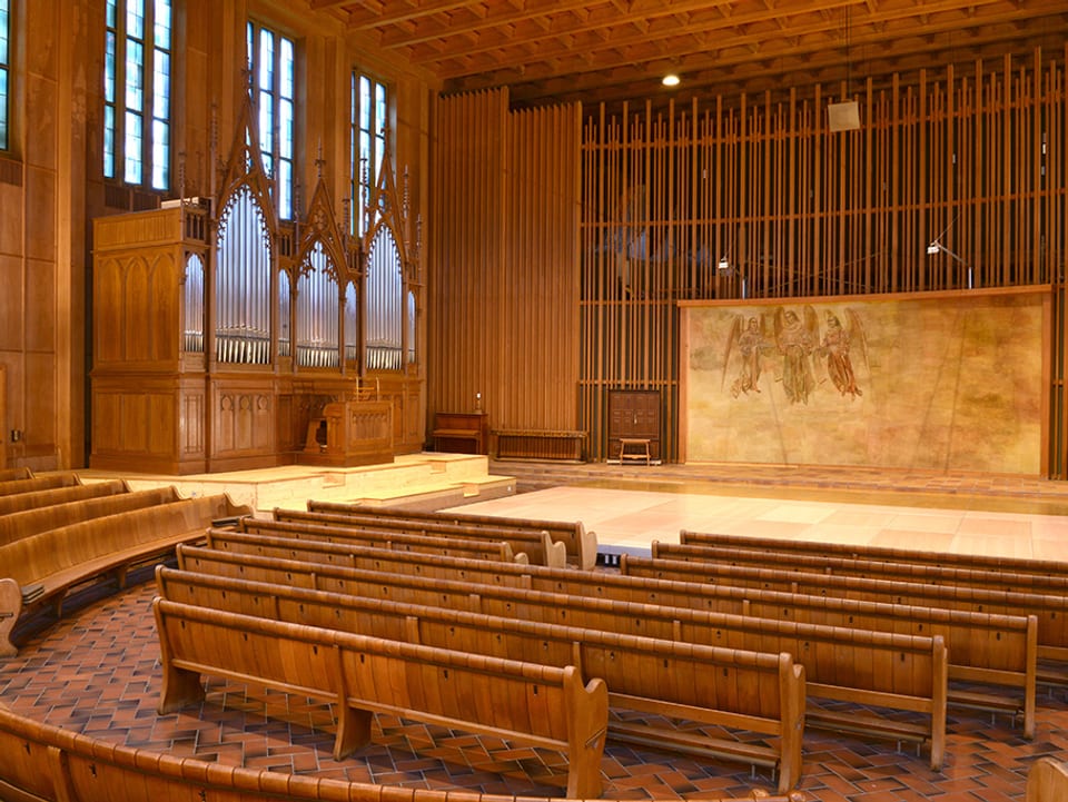 Blick in eine Kirche mit Holzbänken, auf der linken Seite die Orgel.