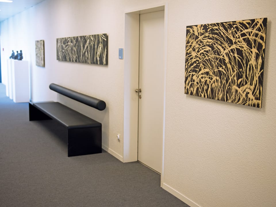 Drei Holzschnitte an einer Wand. Im Hintergrund Skulpturen.