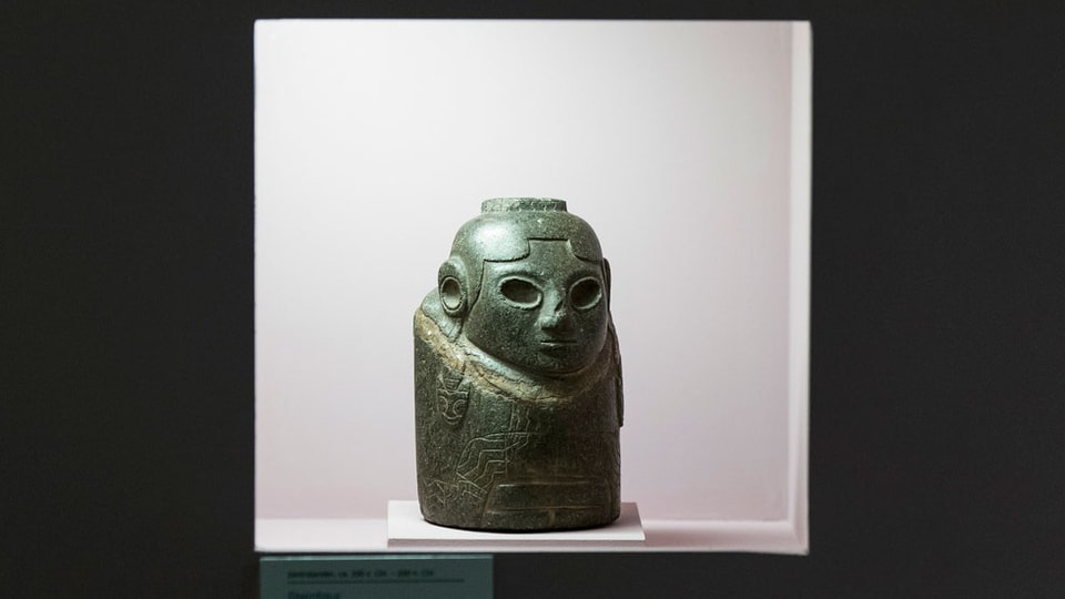 Steinfigur Ekeko steht in einer Museums-Vitrine 