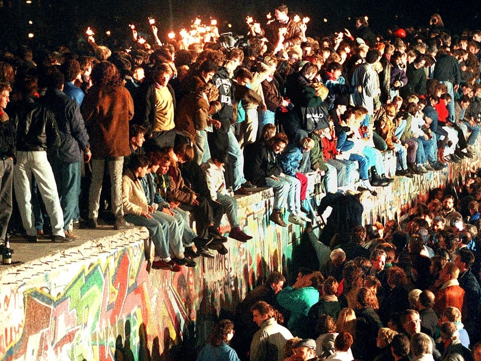 Menschen feiern ausgelassen auf der Berliner Mauer, im November 1989.