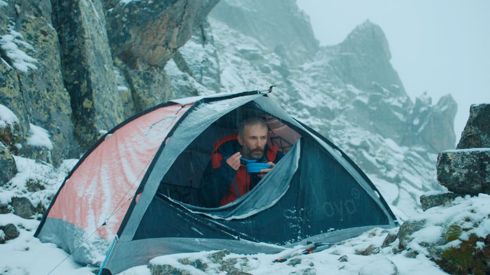 Ein Mann sitzt löffelt im Schneegestöber seine Suppe in seinem kleinen Biwak in den Bergen.
