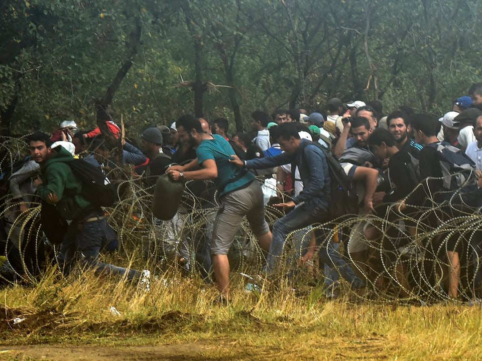 Flüchtlinge zwängen sich durch die Stacheldraht-Absperrung hindurch