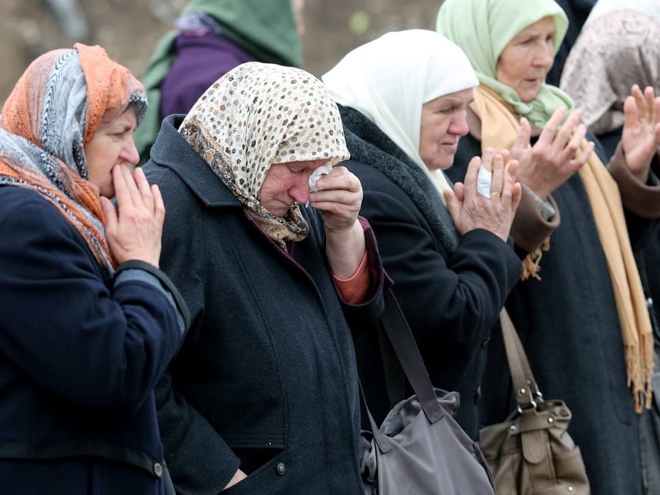 Muslimische Frauen mit Kopftüchern weinen an einem Grab in Srebrenica. 