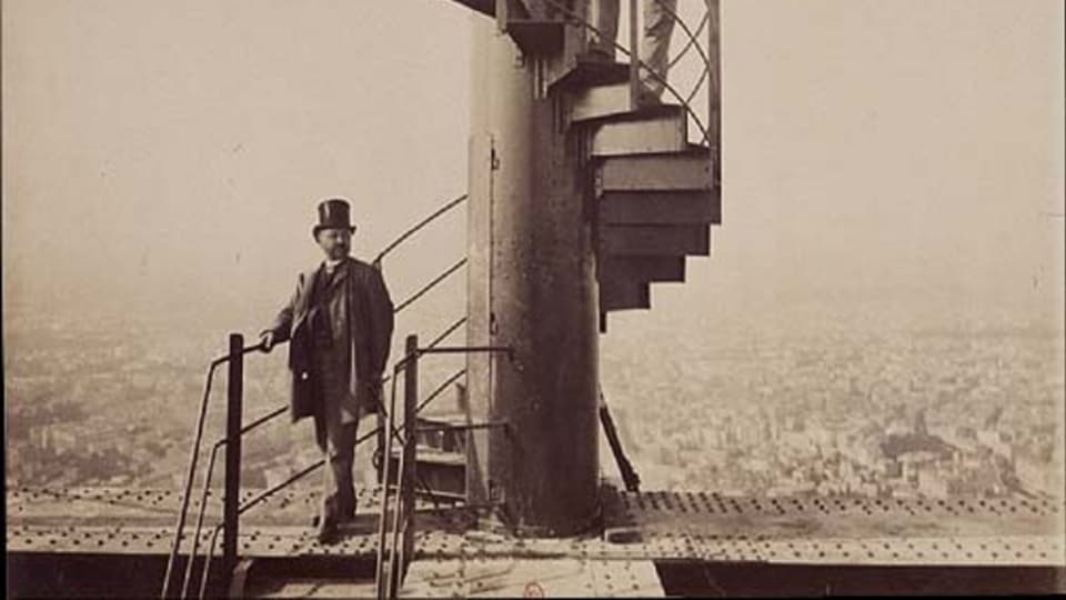 Historische Aufnahme von Gustave Eiffel, der am Fusse des Eiffelturms posiert.