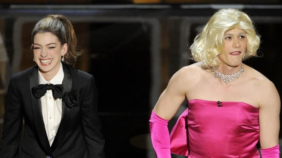 Anne Hathaway laughs alongside James Franco, who is wearing a women's dress.  The two hosted the 2011 Oscars.