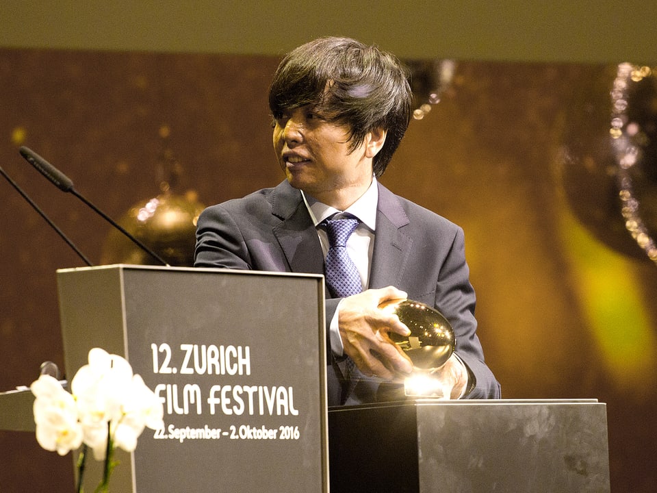 Preisträger Jero Yun nimmt das goldene Auge in seine Hände.
